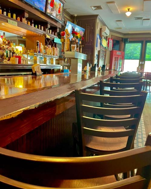 A view of a bar with empty chairs, wooden counter, and TVs displaying drinks in a cozy setting.