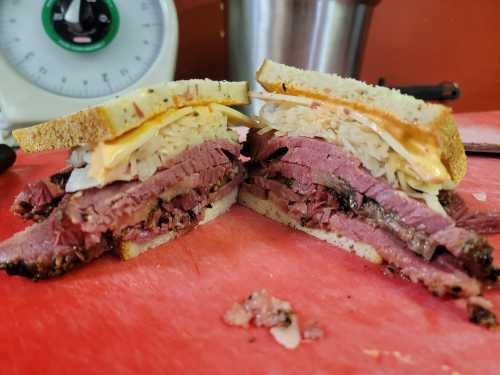 A close-up of a sliced sandwich with layers of meat, cheese, and coleslaw between two pieces of bread on a cutting board.