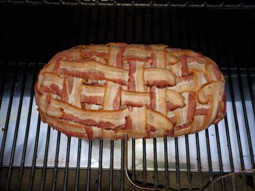 A meatloaf wrapped in a woven layer of crispy bacon, resting on a grill.