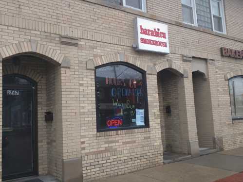 A brick building with a sign reading "Baralich" and colorful hours of operation displayed in the window.