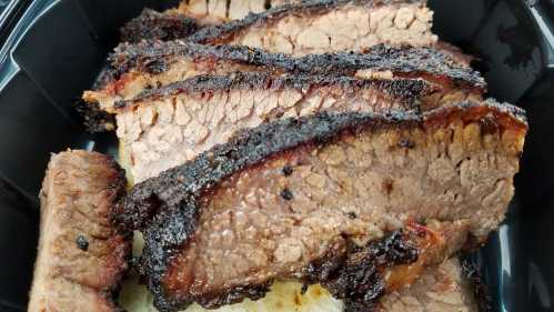 Sliced smoked brisket with a dark, crispy crust, served on a black container.