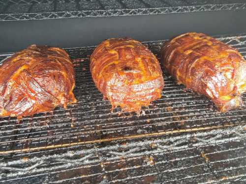 Three smoked meatloafs wrapped in bacon, resting on a grill rack inside a smoker.