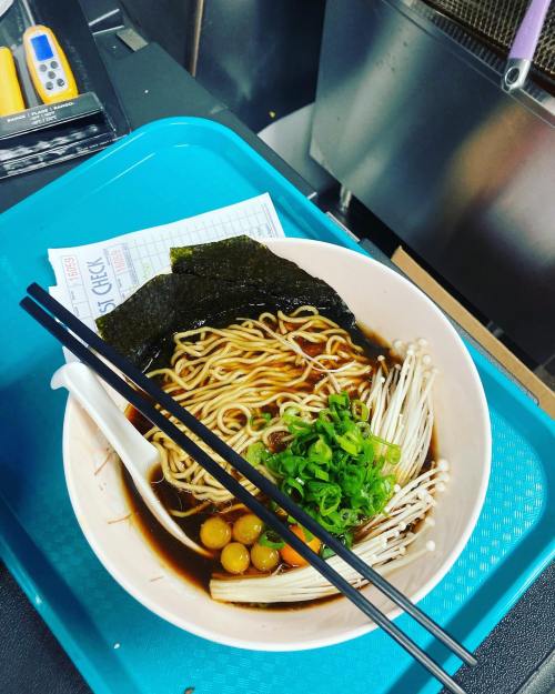 A bowl of ramen with noodles, green onions, mushrooms, and seaweed, served on a blue tray with chopsticks.