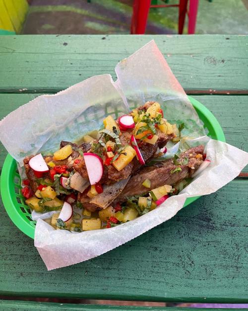 A vibrant dish featuring grilled meat topped with a colorful salsa of radishes, pineapple, and herbs, served in a green basket.