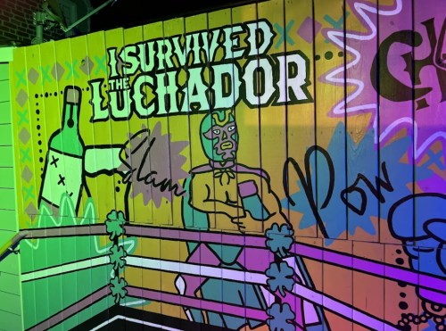 Colorful mural featuring a luchador, graffiti-style text, and playful designs on a wooden wall.