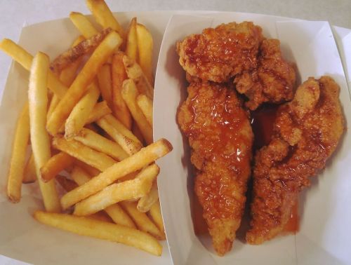 A serving of crispy fried chicken tenders drizzled with sauce, accompanied by a side of golden French fries.