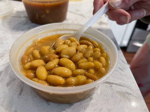 A plastic container filled with yellow beans in a savory broth, with a spoon resting inside.