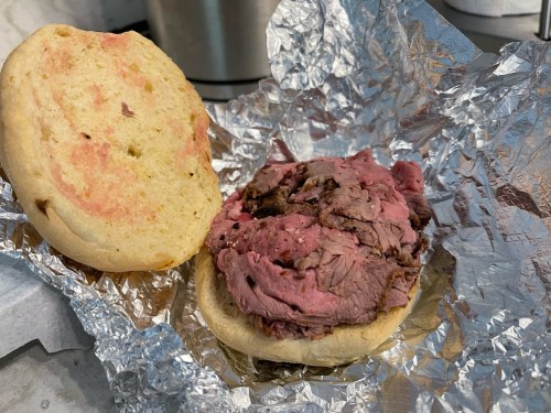 A sandwich with a toasted bun and slices of roast beef, wrapped in foil on a countertop.