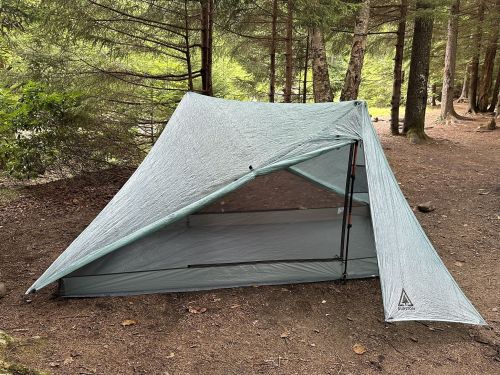 A lightweight tent set up in a forest clearing, surrounded by trees and natural foliage.