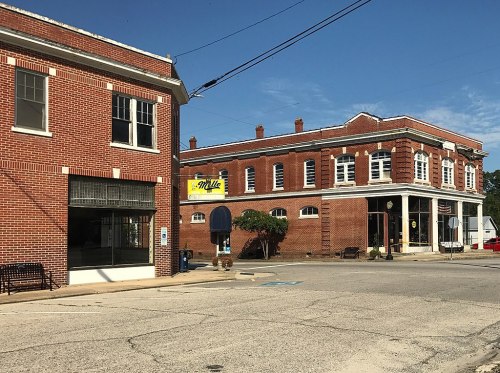 A sunny street view featuring brick buildings, a bench, and a sign for "Milo's" on the corner.
