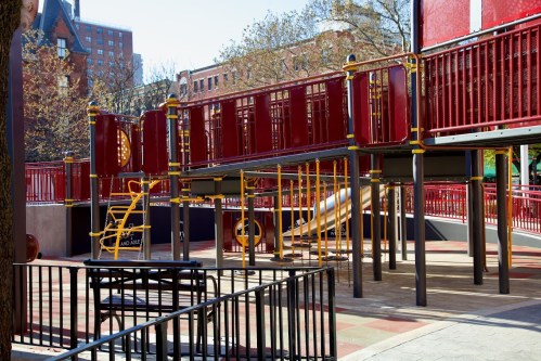 A colorful playground structure with slides and climbing features, surrounded by trees and buildings in the background.