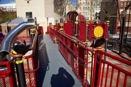 A colorful playground with slides and climbing structures, featuring red and yellow equipment on a sunny day.