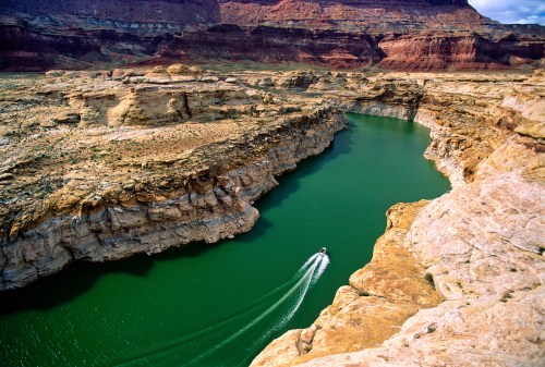 Aerial view of a winding river surrounded by rocky cliffs and vibrant green water in a desert landscape.