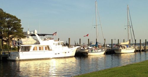 Three boats docked at a marina during sunset, with calm water and trees in the background.