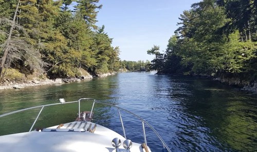 A boat navigating through a serene, tree-lined waterway on a clear day.