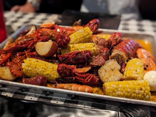 A large tray filled with a variety of seafood, including crawfish, shrimp, corn, potatoes, and sausage.