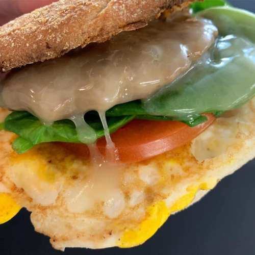 Close-up of a sandwich with a toasted bun, egg, lettuce, tomato, and melted cheese oozing out.