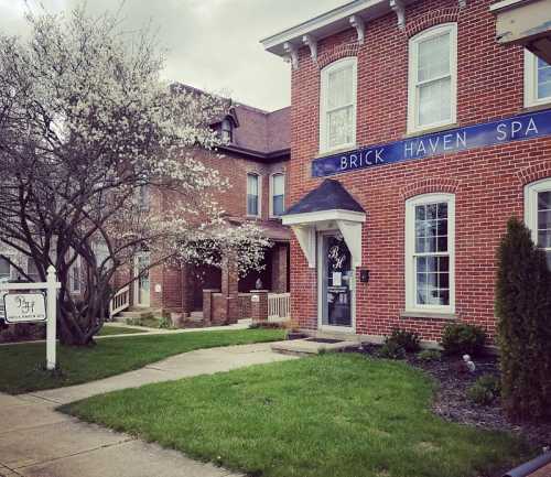 A brick building with a sign reading "Brick Haven Spa," surrounded by greenery and flowering trees.