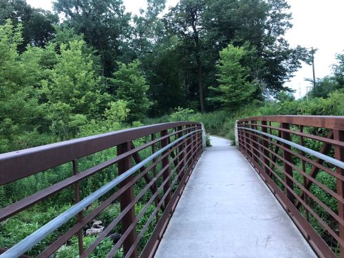A metal bridge over a path surrounded by lush green trees and foliage.
