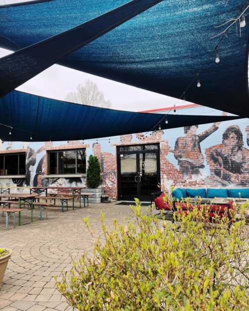 Outdoor seating area with colorful canopies, a mural on the wall, and potted plants in a cozy, inviting atmosphere.