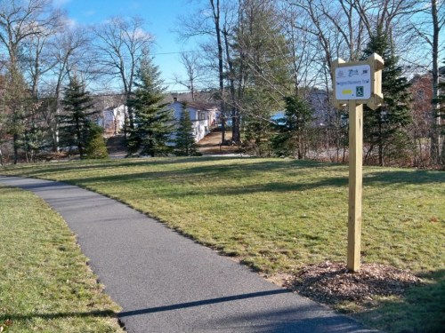 A paved path leads through a grassy area, with a sign for the "Discovery Trail" nearby and trees in the background.