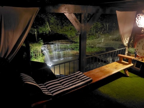 A cozy outdoor seating area with a striped cushion, overlooking a serene waterfall at night.