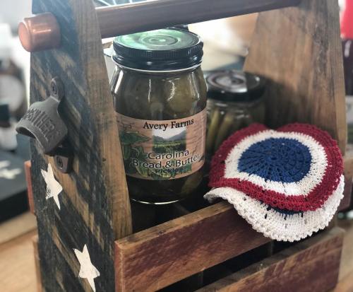 A rustic wooden caddy holds a jar of pickles and a crocheted red, white, and blue coaster.
