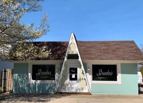 A quaint bakery with a light blue exterior and a brown shingled roof, featuring large windows and a welcoming entrance.