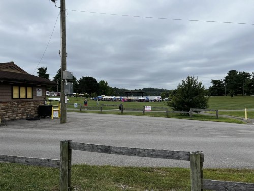 A cloudy day view of a grassy area with tents set up for an event, seen from a nearby road.