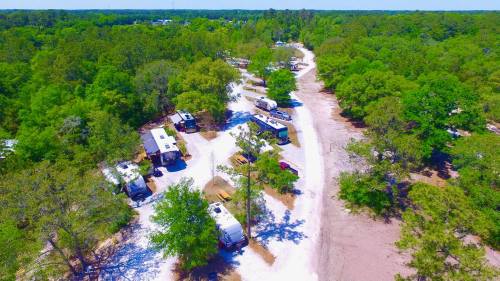 Aerial view of a campground with RVs and trees lining a winding dirt road under a clear blue sky.