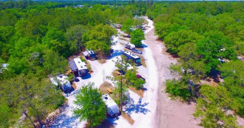 Aerial view of a campground with RVs and trees along winding paths in a lush green setting.