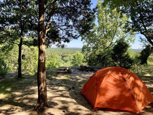 An orange tent set up in a wooded area, overlooking a scenic view of trees and hills in the distance.