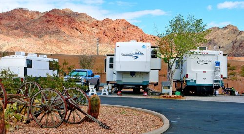 A scenic RV park with white trailers, a pickup truck, and desert mountains in the background.