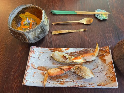 A plate with two crab claws, a bowl with colorful garnish, and elegant utensils on a wooden table.