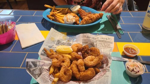 A plate of fried shrimp and fries with a lemon wedge, alongside another plate of fried fish and coleslaw.