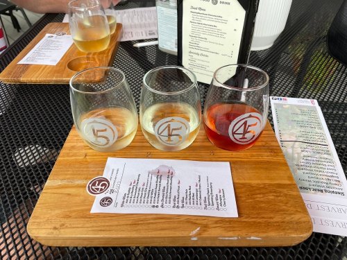 Three wine glasses on a wooden tray, filled with white, rosé, and red wine, alongside a menu on a table.