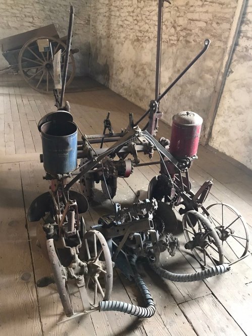 An old farming machine with wheels and metal components, resting on a wooden floor in a rustic setting.