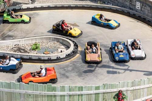 Go-karts racing on a circular track with colorful cars and excited drivers enjoying a fun day at an amusement park.