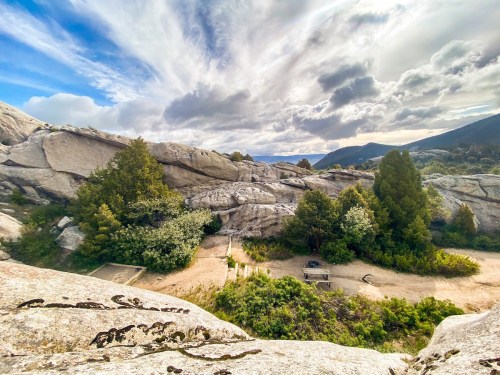 A scenic view of rocky terrain with trees and a path, under a cloudy sky.