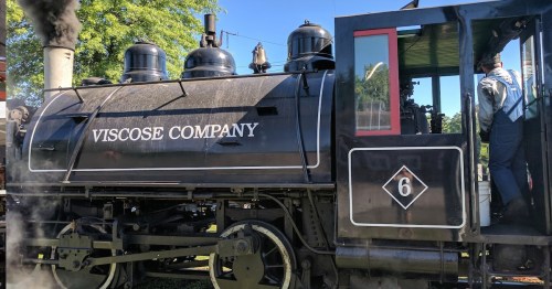 A vintage steam locomotive with "VISCOSE COMPANY" written on the side, surrounded by greenery.