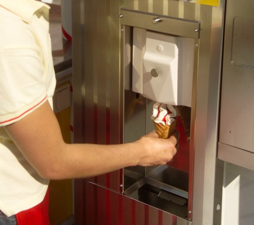 A person holds a cone while dispensing soft serve ice cream from a machine.