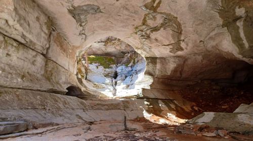 A rocky cave with a circular opening, allowing light to filter through onto the stone floor.