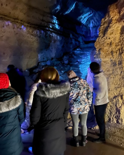 A group of people exploring a cave with blue lighting reflecting off the rocky walls.