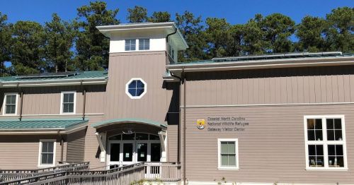 Exterior of a modern visitor center with a green roof, surrounded by trees and featuring a large window.