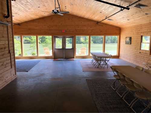 Interior of a wooden meeting room with tables, chairs, and large windows overlooking a lake.