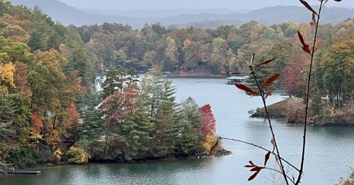 A serene lake surrounded by colorful autumn trees and distant mountains under a cloudy sky.