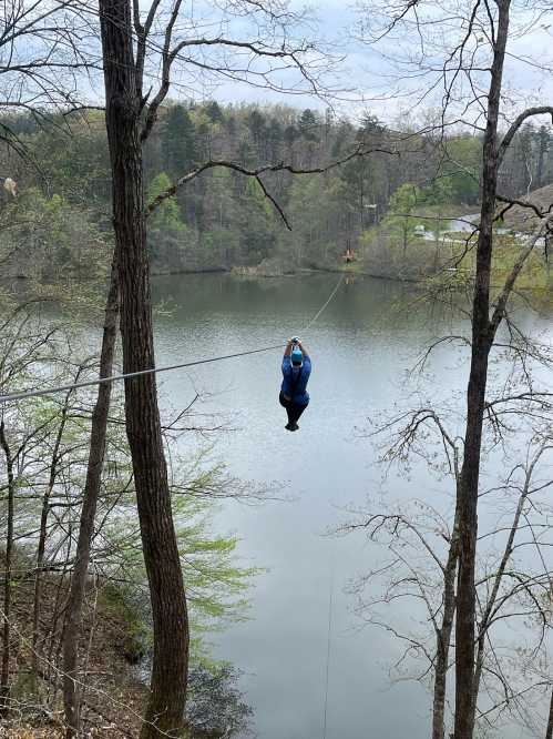 A person in blue gear zip-lining over a calm lake surrounded by trees and greenery.