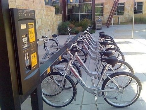 A row of parked bicycles at a bike-sharing station with a payment kiosk nearby.