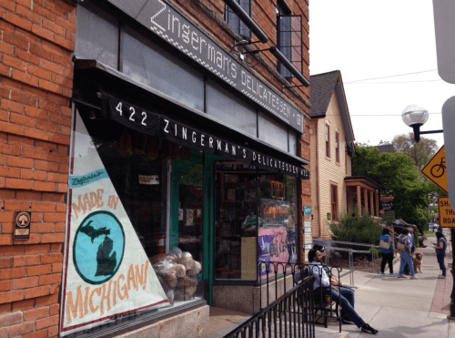 A brick building with a sign for Zingerman's Delicatessen, featuring a "Made in Michigan" window display.