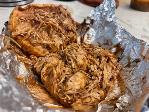 Shredded chicken in barbecue sauce served in foil, with a soft bun on the side.